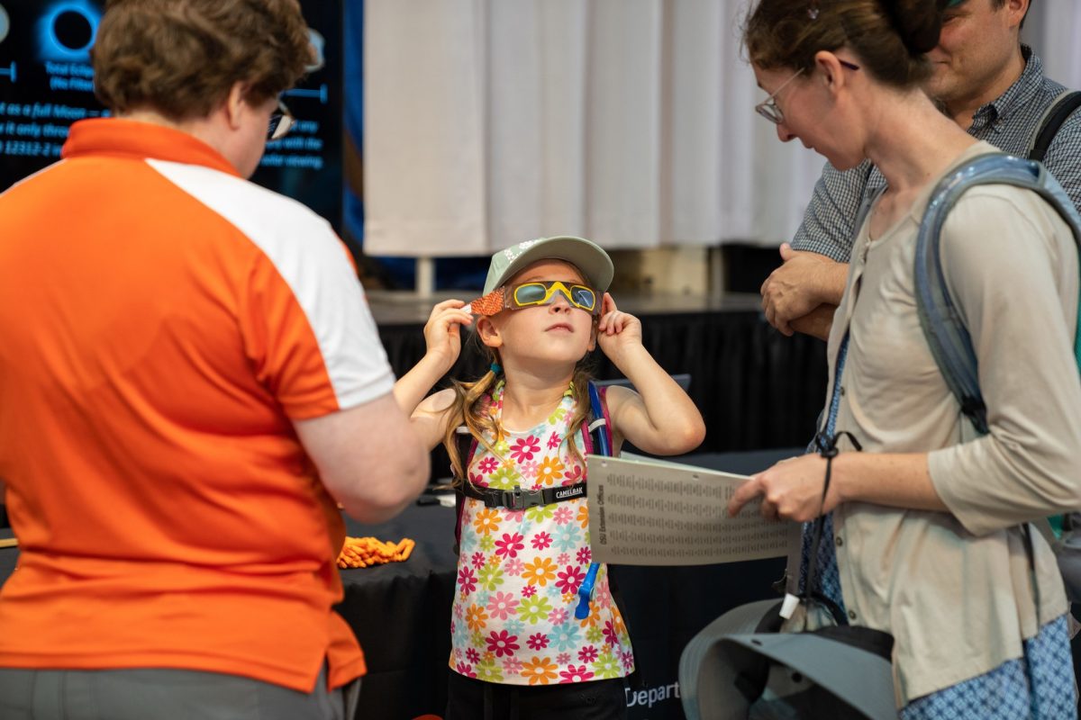 BGSU Department of Physics and Astronomy Professor Dr. Kate Dellenbusch looks on as a young fairgoer peeks through Falcon-themed eclipse glasses at the Ohio State Fair. 