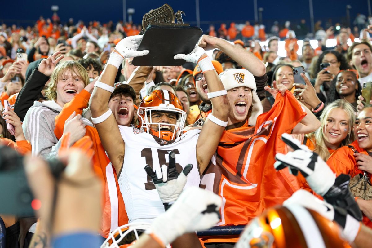 Toledo, OH - Falcons senior outside linebacker Avi McGary (15) holds the Battle of I-75 trophy high surrounded by BGSU students after defeating the Rockets of the University of Toledo at the Glass Bowl in Toledo, Ohio.