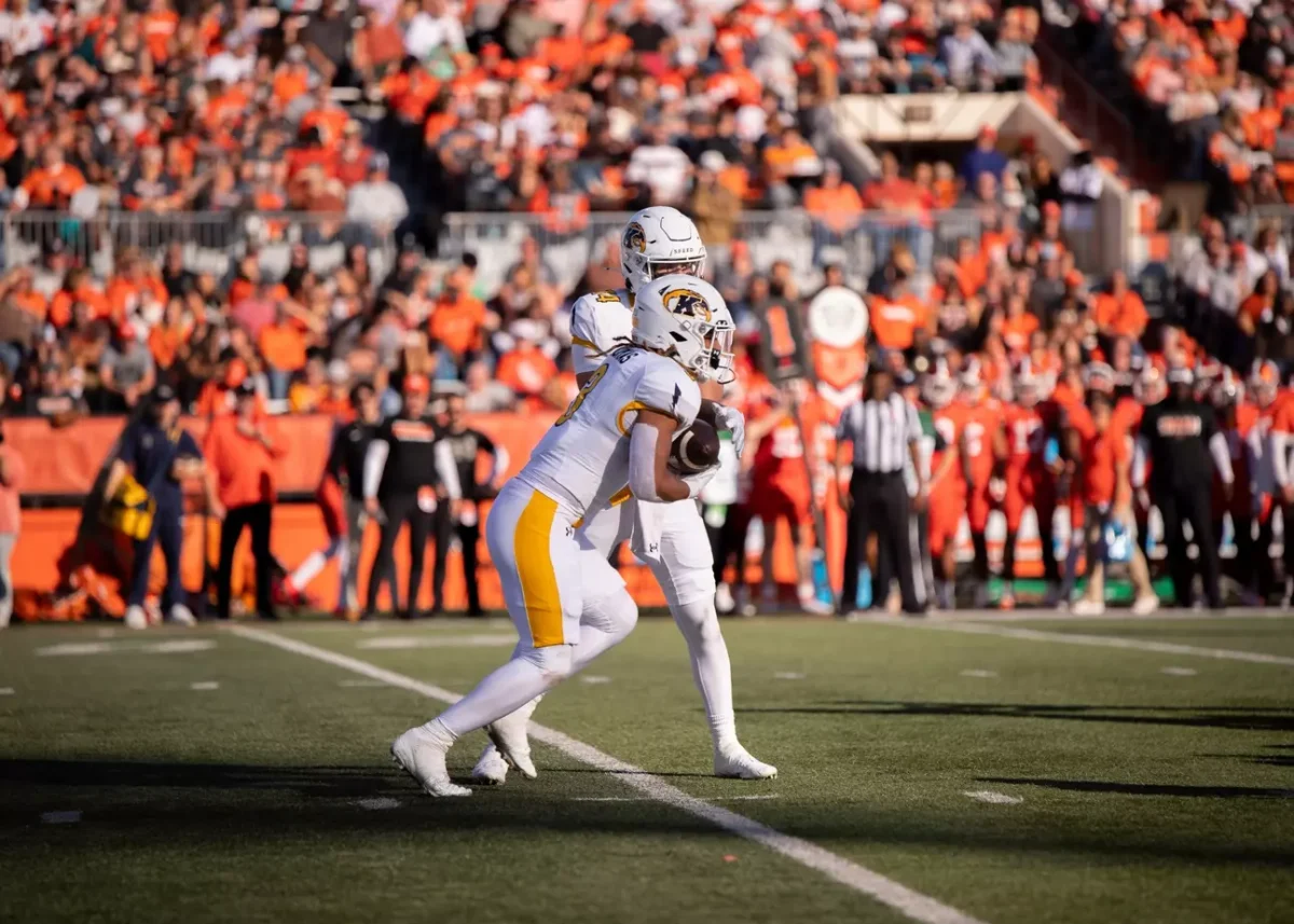 Kent State players hand off ball in front of a sea of orange and brown. 