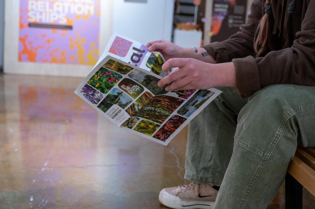 Student holding an In the Roots paper at the exhibit