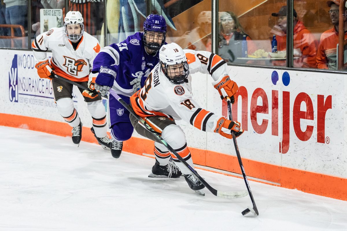 Bowling Green, OH - Falcons senior forward Quinn Emerson (18) looks to outskate Tommies senior defenseman Carson Peters (21) with the puck during a game between the St. Thomas Tommies and the Bowling Green Falcons at the Slater Family Ice Arena.